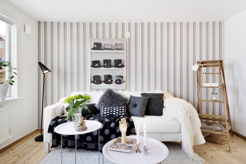 Czarna lampa podłogowa,tapeta w szare paski,biała sofa i okrągłe stoliki kawowe z tacą