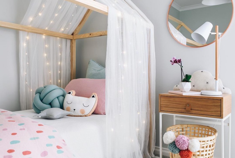 Łóżko domek z tiulem i girlandą świetlną w pokoju dziecięcym
