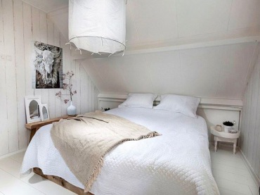 W sypialni na poddaszu drewno na podłodze oraz ścianie nawiązuje do naturalnego stylu rustykalnego. Znajduje się tu...