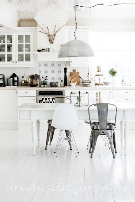Tradycyjna biała kuchnia skandynawska z białym stołem na toczonych nogach,lampą z ocynku i mieszanymi krzesłami w stylu nowoczesnym i industrialnym