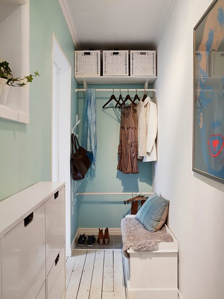 Niebiesko-turkusowa ściana,biale kosze pojemniki z wikliny,wąska szafka wisząca na buty,biała szafka skrzyniowa na podlodze i kolorowy nowoczesny plakat na ścianie