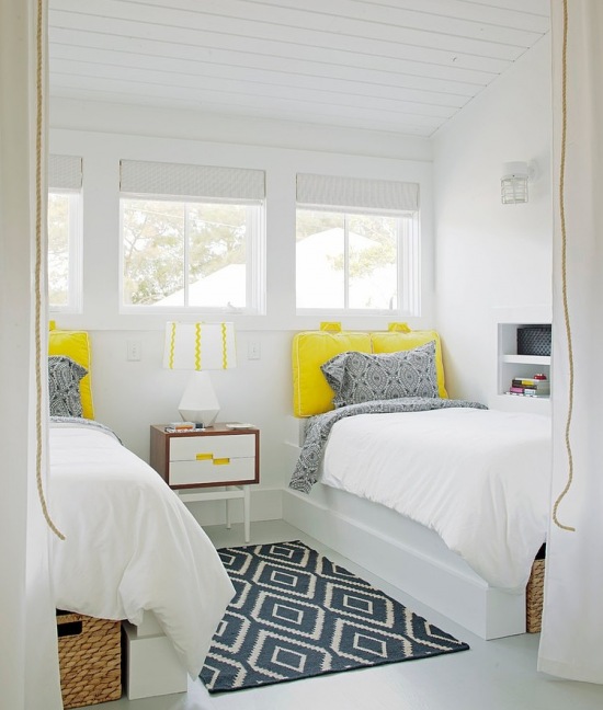 Biała sypialnia zszaro-białym dywanem w geometryczne wzory i żółtymi zagłówkami przy łóżku