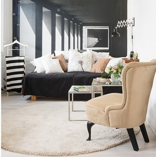 Karmelowy fotel uszak i karmelowe poduszki na czarnej sofie w salonie z czarno-białą fototapetą na ścianie