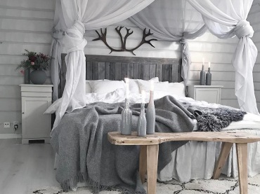 Ciemne poroże nad łóżkiem i biały tiulowy baldachim przeciwstawiają się sobie pod względem stylu. Tworzą w ten sposób...