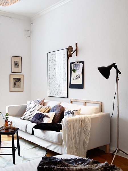 Biała sofa,czarna lampa podłogowa,mały stolik kawowy i grafiki