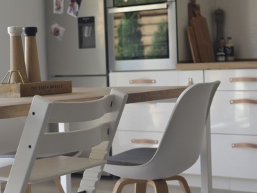 Białe krzesła przy drewnianym stole potęgują wrażenie przytulności i domowego ciepła. Otwarta kuchnia harmonijnie...
