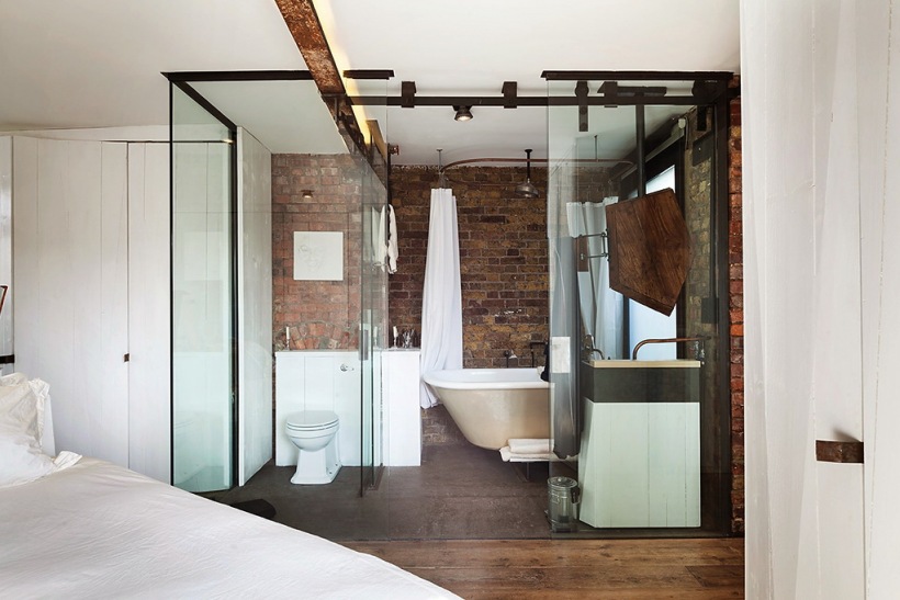 Białą sypialnia z łazienką ze szklanymi ścianami i ścianami z czerwonej cegły