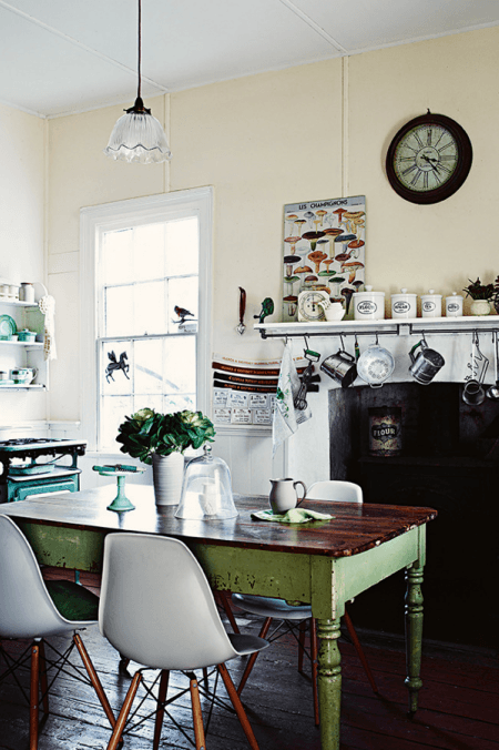 Zielony stół vintage z drewna,nowoczesne krzesła VITRA i wiejski kominek z wiszącymi kuchennymi akcesoriami