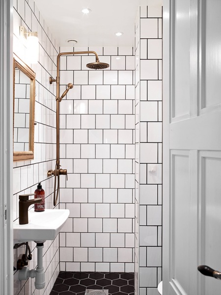 Białe kwadratowe kafeki na ścianie, czarne sześciokątne na posadzce w łazience z miedzianym prysznicem retro