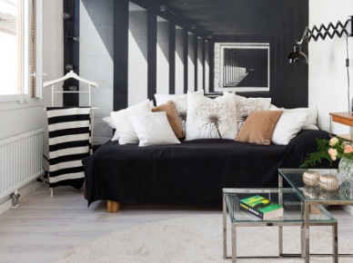 Czarna sofa z białymi i jasno-brązowymi poduszkami na tle ściany z fototapetą,metalowe kwadratowe stoliki ze szkłem i jasna podłoga z drewna w salonie (26261)
