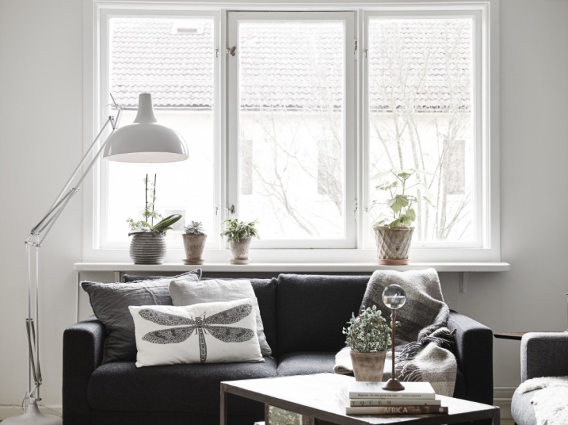 Biała lampa podłogowa,czarna sofa,graficzne poduszki z ważką i stolik pomocniczy w salonie