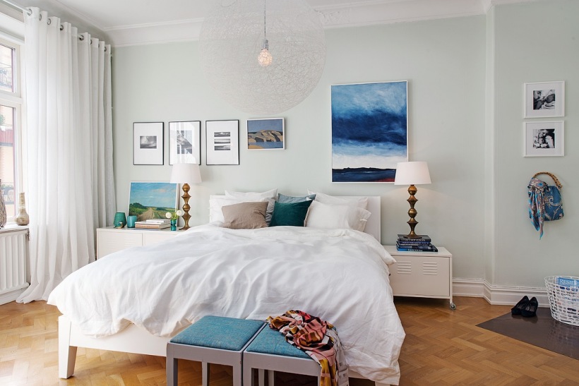 Niebieskie obrazy,nowoczesne ilustracje i białe szafki w aranżacxji skandynawskiej sypialni