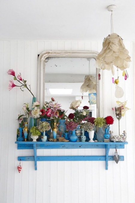 Niebieska półeczka z białym lustrem i z niebieskimi wazonikami i kwiatami