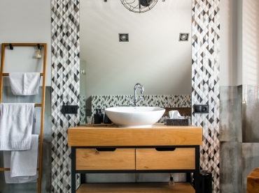 W łazience niektóre fragmenty ścian są wyłożone płytkami z geometrycznym wzorem. Aranżacja przestrzeni wokół umywalki...