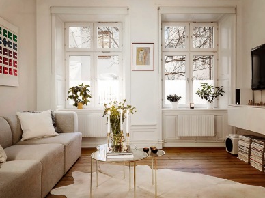 Nowoczesna sofa modułowa,okrągłe złote stoliki ze szklanymi blatami,wisząca biała szafka tv i biały dywan z bydlęcej skóry na drewnianej podłodze w salonie skandybnawskim (27096)