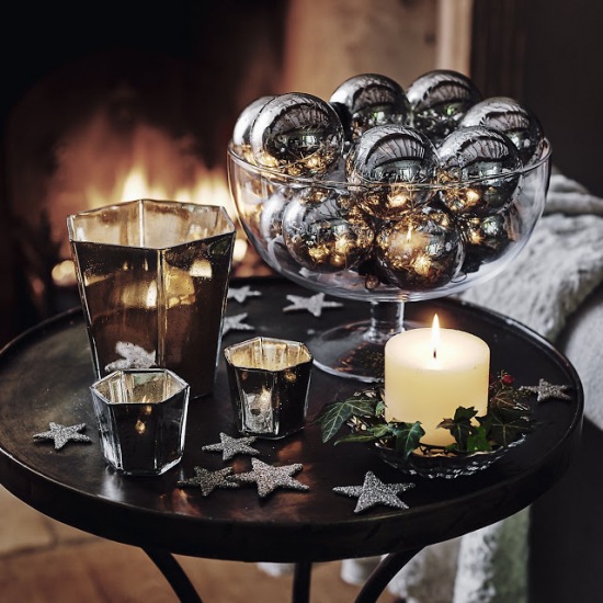 Okrągły stolik przy kominku w świątecznej dekoracji ze srebrnymi bombkami i gwiazdkami