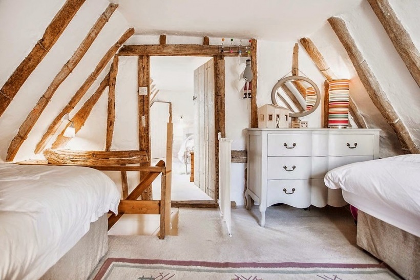 Sypialnia dla gości na poddaszu z drewnianymi belkami,okrągłym lustrem i francuska komodą