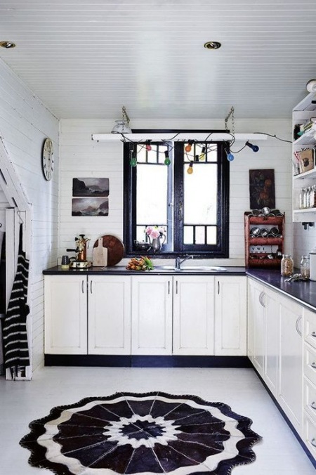 Czarny ornament na białej podłodze w kuchni,białe szafki,czarne okno i dodatki i kolorowa girlanda z żarówkami nad oknem kuchennym