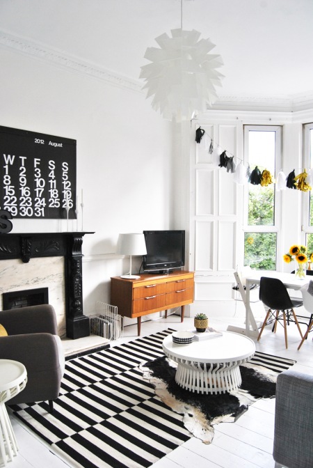 Czarny portal kominkowy,dywan w paski,skóra bydlęca i nowoczesne meble w salonie