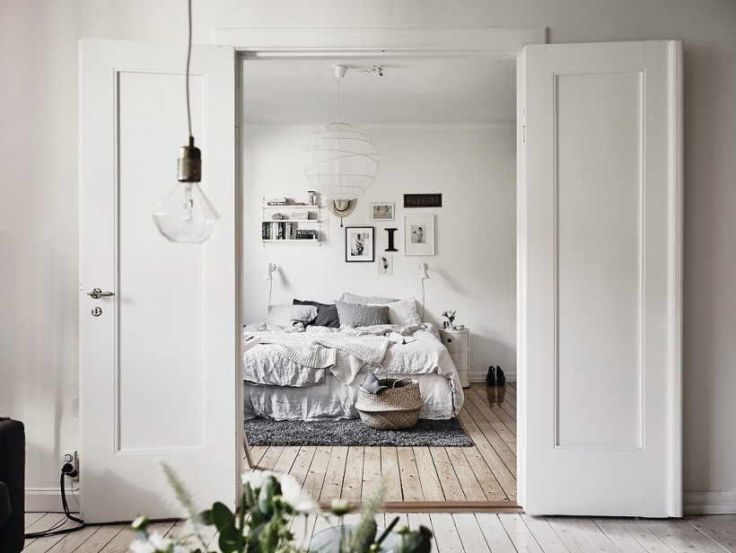 Bielone deski na podłodze,nowoczesne grafiki na białej ścianie i białe drewniane dwuskrzydłowe drzwi w sypialni