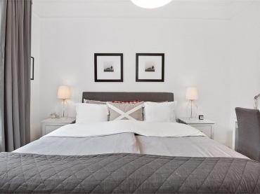 Symetryczna aranżacja sypialni kojarzy się z ładem i harmonią. Czarne dodatki w wyraźny sposób dekorują wnętrze, podkreślają jego poważny charakter. Szarą pościel i narzutę dopasowano do ramy łóżka o podobnym...