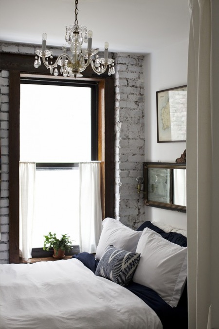 Biała cegła, kryształowy żyrandol i ciemne drewniany ramy okien w sypialni