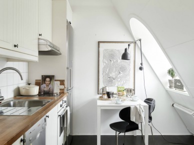 Biała kuchnia z drewnianym blatem, kwadratowy biały stolik z czarnymi krzesłami,grafitowy kinkiet z wysięgnikiem i czarna podłoga w kuchni (27323)