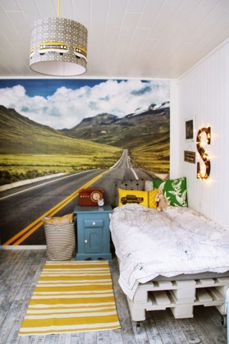 Żółte poduszki i dywanik w żółte paski w dekoracji pokoju dla dziecka z łóżkiem na drewnianych paletach