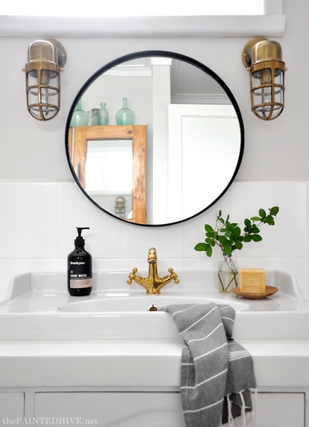 Okrągłe lustro ze złotymi kinkietami w aranżacji łazienki