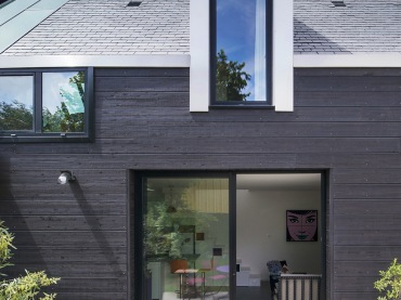 typowy skandynawski mały domek w szeregowej zabudowie - czarna elewacja z desek,wewnątrz białe ściany, a na podłodze...