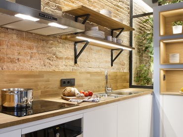 W aranżacji kuchni skupiono się na połączeniu piaskowych cegieł na ścianie z drewnianymi deskami na suficie. Dla...
