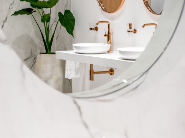 Okrągłe lustro stanowi prostą, ale wyraźną dekorację w łazience. Biały kamień z szarymi smugami prezentuje się...