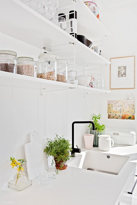 Białe szafki, białe wiszące półki i białe blaty w kuchni w stylu skandynawskim