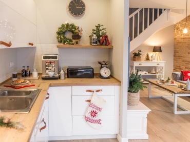 Otwarta drewniana półka w białej kuchni dodaje jej lekkości. Paleta barw tworzy klimat skandynawski.