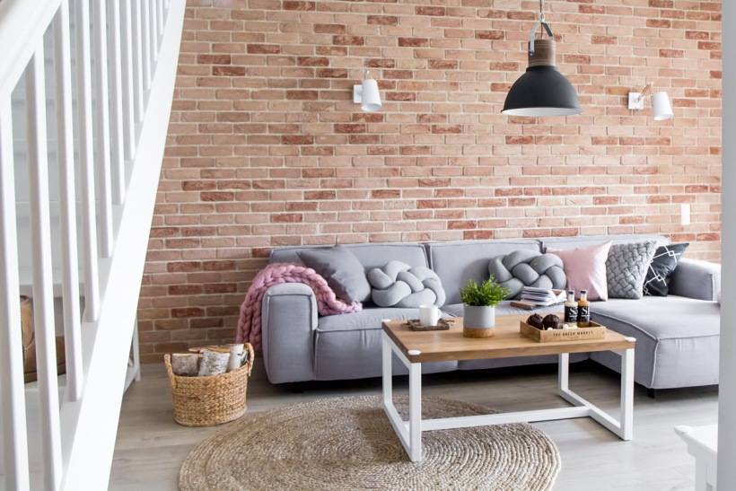 Czerwone cegły i szara sofa w salonie