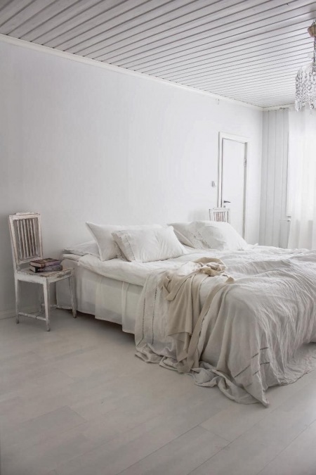 Biała sypialnia z patynowanym krzesłem, kryształowym żyrandolem i białą dekoracją łóżka