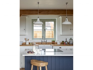 Białe meble i drewniany blat kuchenny na tle białych ścian to idealne połączenie. Do tego wyspa kuchenna jako jedyny kolorowy element w tym...