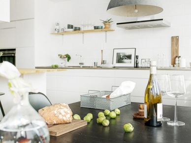 Czarny stół w białej kuchni,szara lampa w stylu industrialnym,czarne kinkiety i drewniane półki na ścianie (28447)