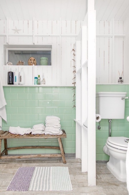 Miętowy kolor ceramicznych płytek na ścianie w białej łazience z ażurową ścianką