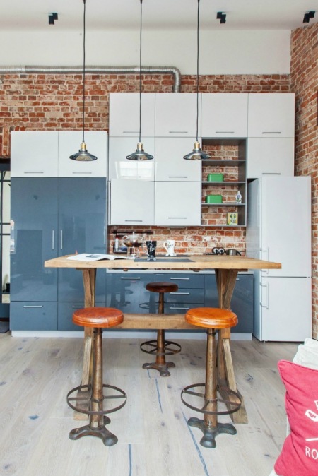 Biało-niebieska kuchnia nowoczesna z industrialnymi lampami,drewnianym stołem i ścianami z czerwonych cegieł