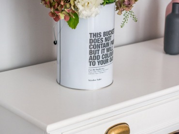 W roli wazonu dobrze sprawdza się ozdobna puszka, którą udekorowano napisami. Kwiaty są w niej ładnie wyeksponowane, a...