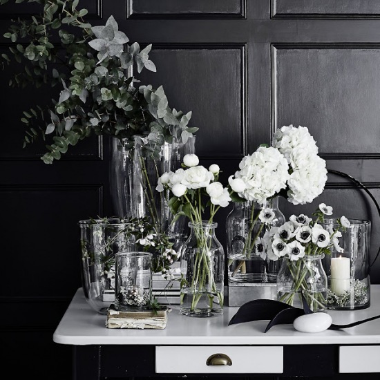 Szklane wazony i butelki z białymi kwiatami do kącika biurowego z czarnymi ścianami
