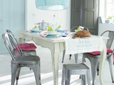 Prowansalski biały stół z drewna,szare krzesła i stołki industrialne z różowymi siedziskami,szara szafa i niebieska lampa nad stołem (27714)