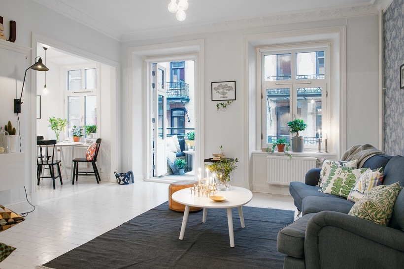 Szara sofa,szary dywan i okragły biały stolik kawowy w salonie skandynawskim