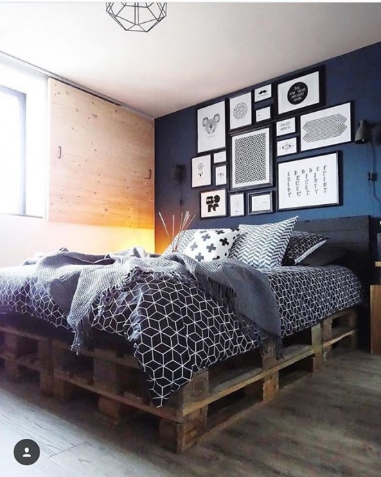 Łóżko z palet i galeria grafik na granatowej ścianie w sypialni