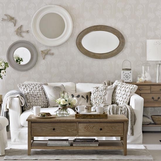 Szare i białe lustro okragłe,owalne lustro w drewnianej ramie,biała sofa,marokański lampion i tradycyjny drewniany stół ława z szufladami w salonie