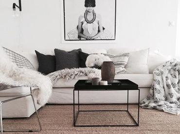 W salonie przed sofą ustawiono geometryczny stolik kawowy z blatem w formie tacy. Jego czarny kolor zwraca na siebie uwagę i nawiązuje do innych dodatków, np. do kinkietu czy fotografii na...