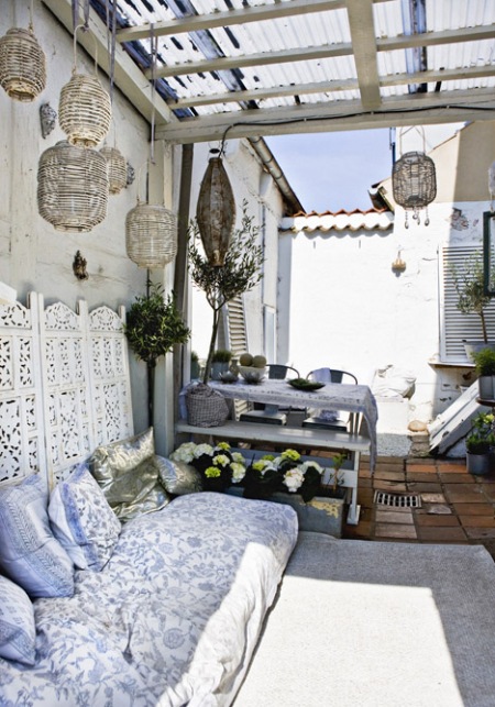 Wiszące lampiony na drewnianej pergoli,biało niebieskie poduszki i ażurowe dekory w marokańskim stylu na tarasie