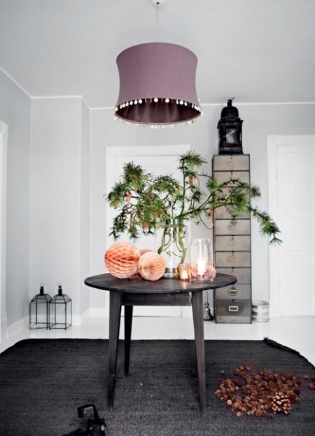 Metalowo-szklane lampiony i latarnie,brązowo-miodowe papierowe kule,zielone drzewko i lampa z paciorkami  nad okragłym drewnianym stołem