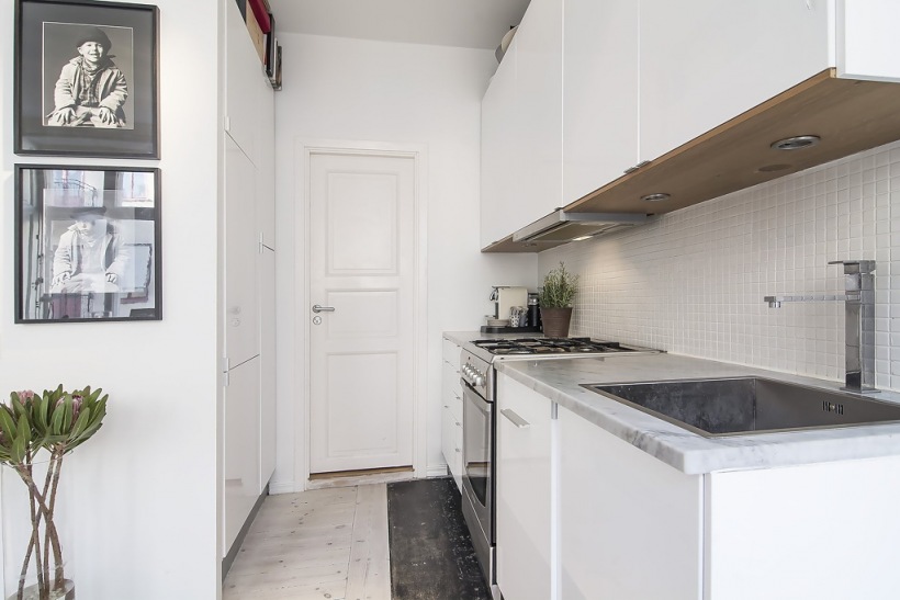 Biała wąska kuchnia z zabudowaną szafą i pomysłową podłogą w dwóch kolorach